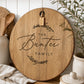 Custom engraved round acacia cheeseboard personalised with a family name, styled in a warm modern farmhouse kitchen.