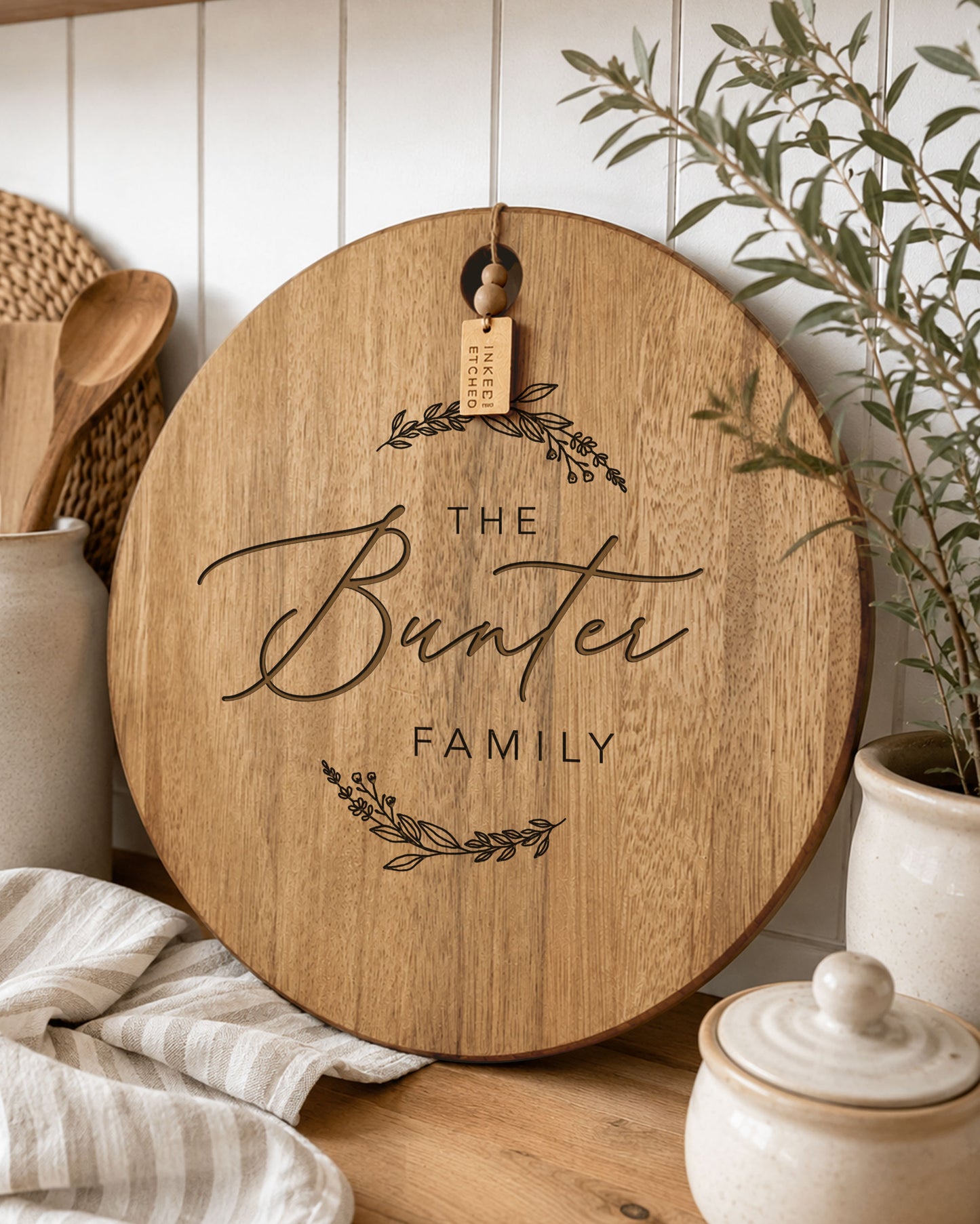 Custom engraved round acacia cheeseboard personalised with a family name, styled in a warm modern farmhouse kitchen.