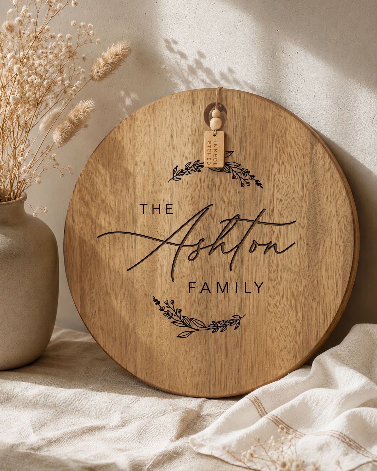 Personalised round acacia serving board engraved with a custom family name, styled with neutral home décor in soft natural light.