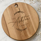 Personalised engraved acacia cheeseboard with custom family name, photographed on a marble surface with baby's breath flowers.