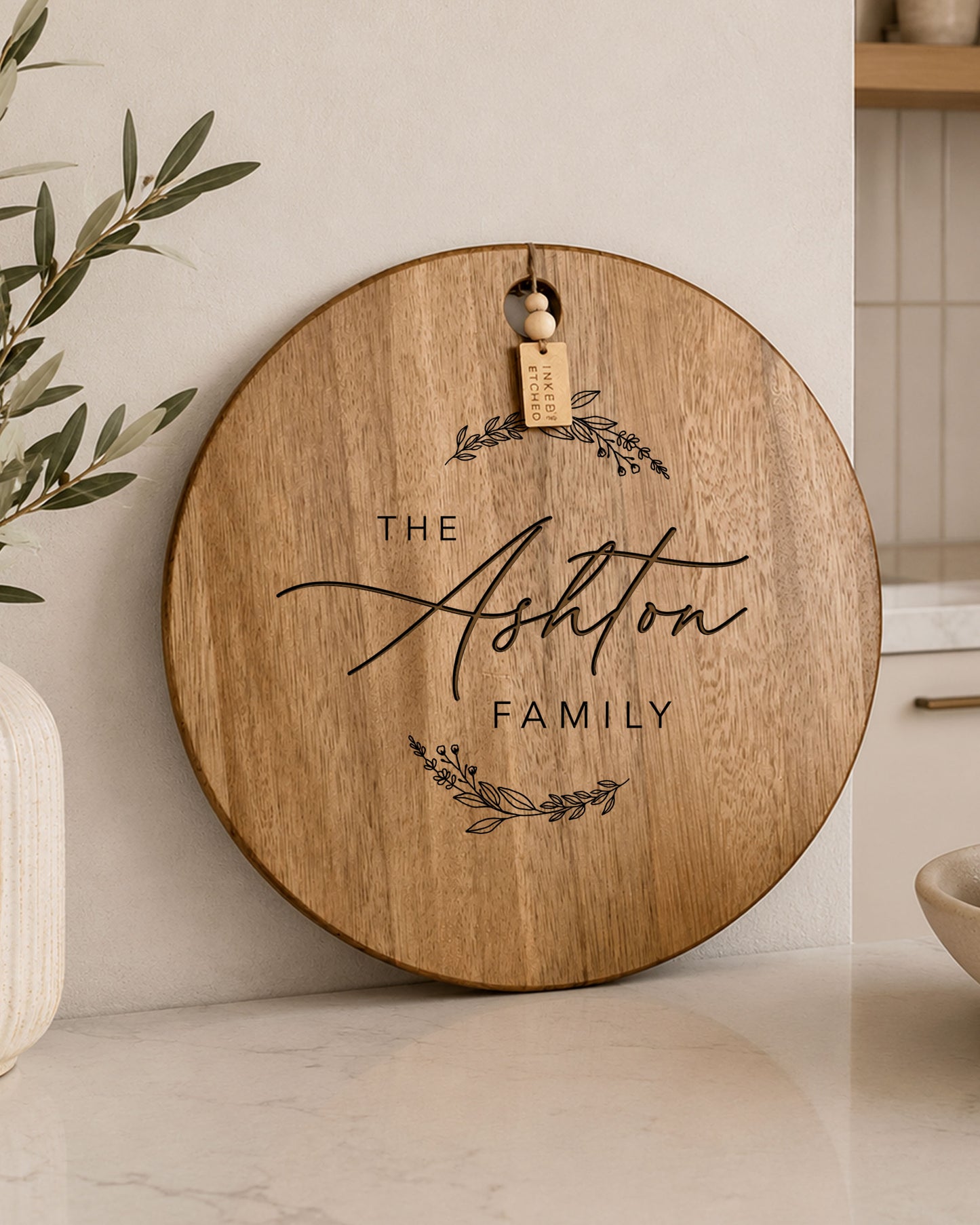 Personalised acacia serving board engraved with family name, displayed on a modern kitchen bench with decorative timber tag.