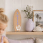 Personalised wooden surfboard wall decor with lavender name Adele and white hibiscus flower displayed on a shelf in a coastal girls bedroom.