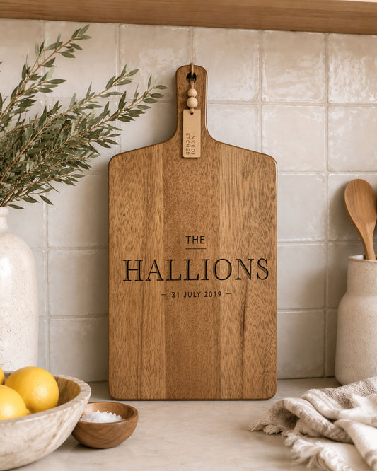 Custom cutting board engraved with family name and established date, made from premium acacia timber and displayed in a modern kitchen. Personalised serving board perfect as a wedding gift, housewarming present or custom kitchen décor.