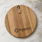 Flat lay of a round acacia serving board laser engraved with the SlaterAir business logo.
