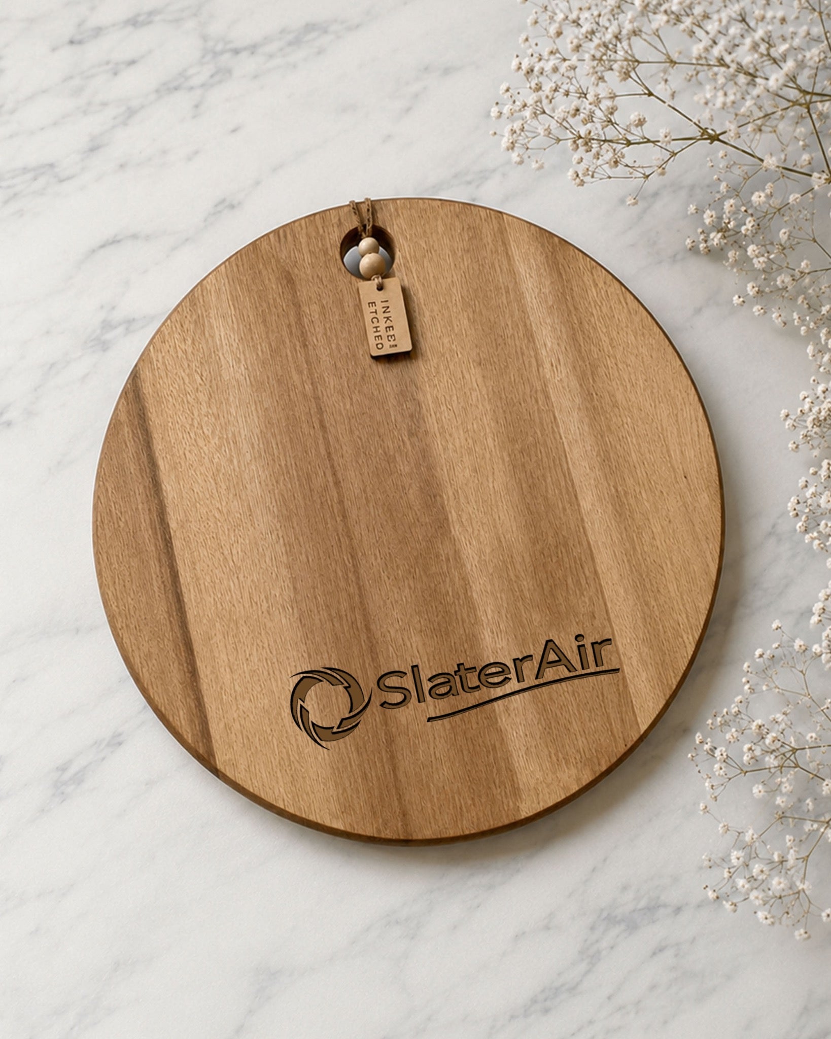 Flat lay of a round acacia serving board laser engraved with the SlaterAir business logo.