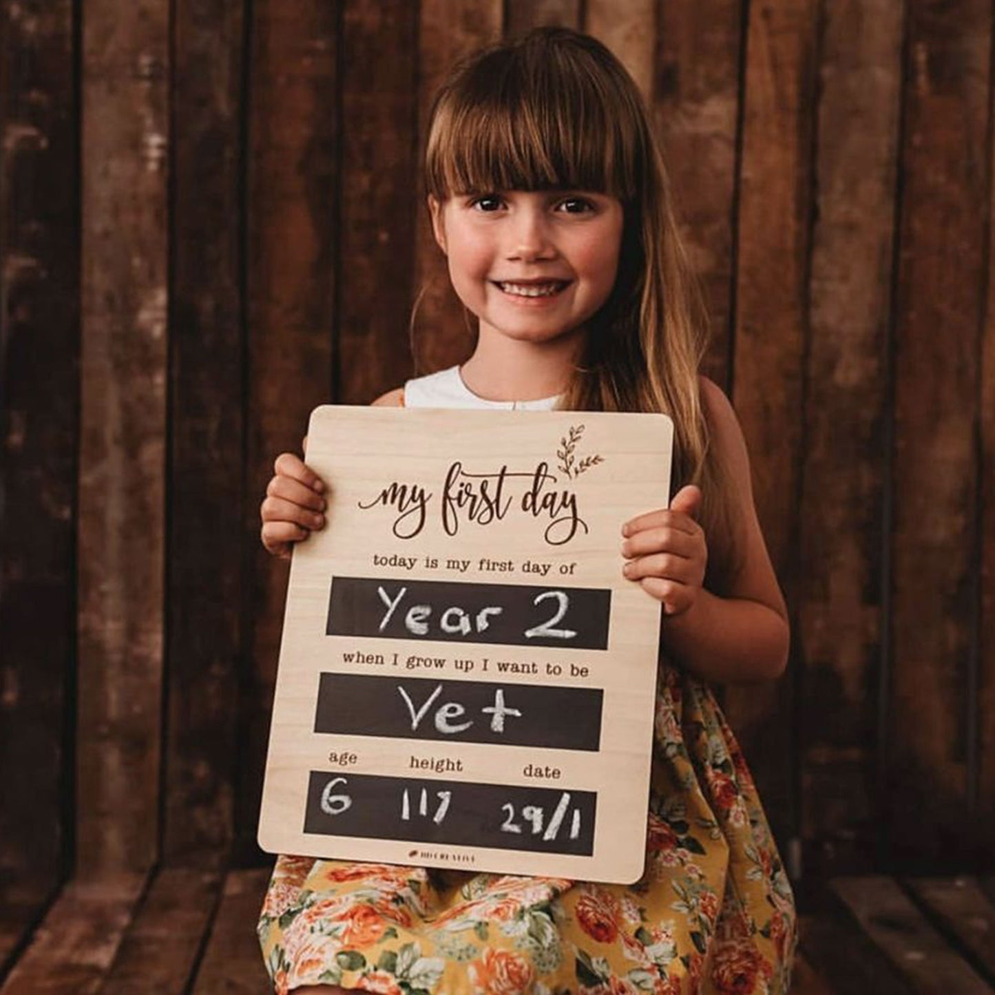 Girl holding a reusable wooden first day of school chalkboard filled in for Year 2.
