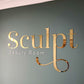 Gold mirror acrylic logo sign installed on a feature wall for luxury beauty business branding.