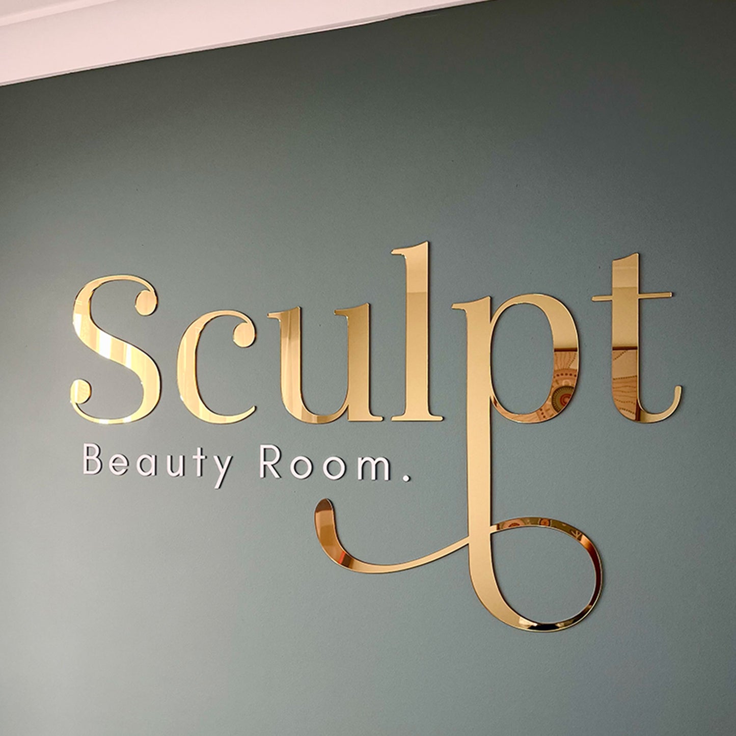 Gold mirror acrylic logo sign installed on a feature wall for luxury beauty business branding.