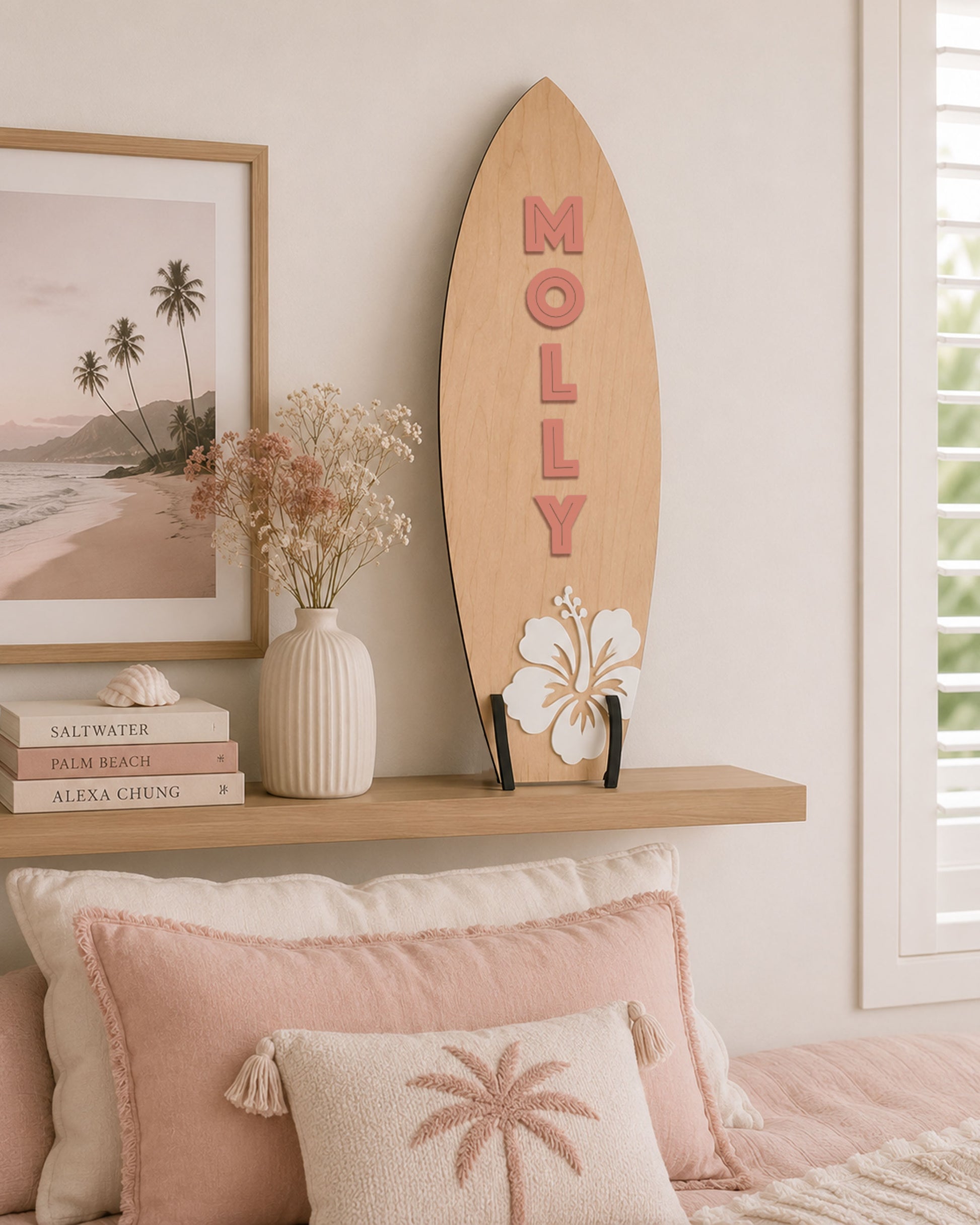 Large personalised wooden surfboard wall decor with hibiscus flower displayed on a shelf in a coastal style children's bedroom. The surfboard is on a shelf above a bed.