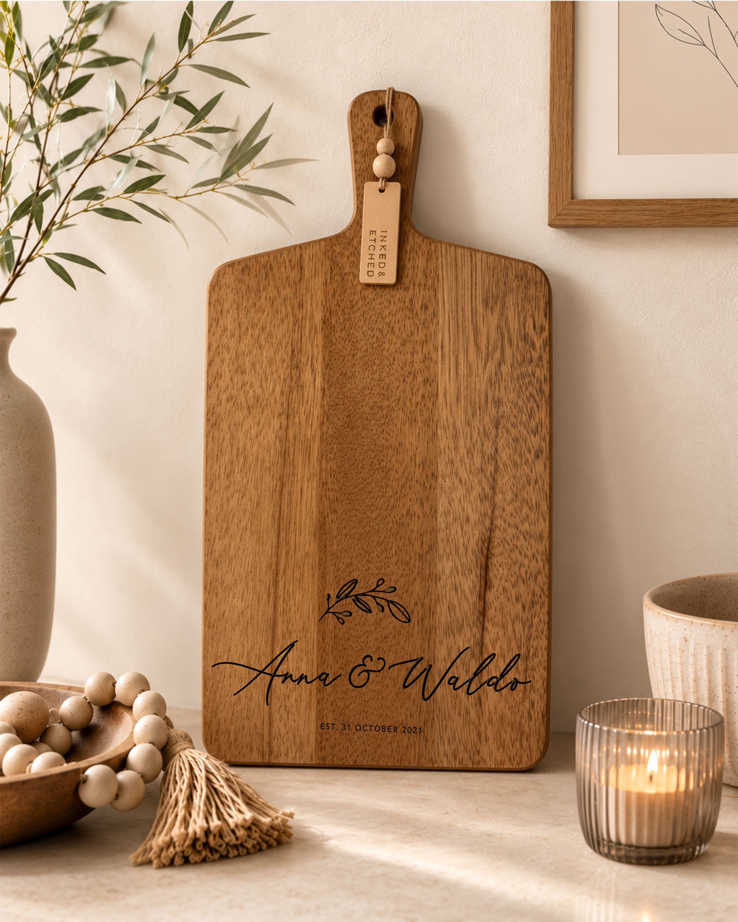 Personalised acacia serving board engraved with names and wedding date displayed in a modern neutral kitchen with candle and timber décor.