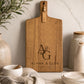 Personalised acacia paddle serving board with engraved initials displayed on a marble kitchen benchtop.
