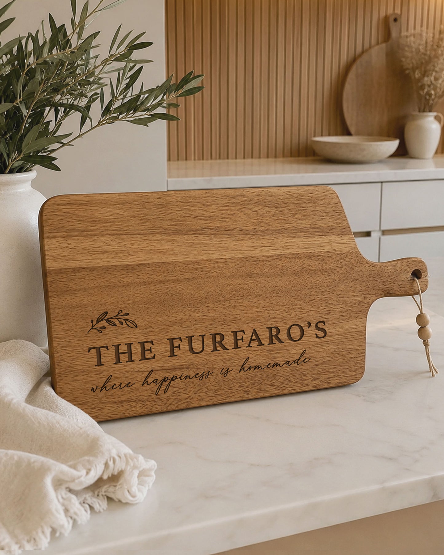 Personalised chopping board engraved with family name on premium acacia timber, displayed on a modern kitchen benchtop with neutral décor.
