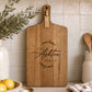 Personalised engraved acacia serving board displayed in a modern kitchen with custom family name engraving.