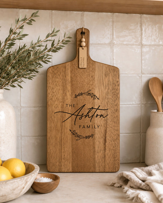 Personalised engraved acacia serving board displayed in a modern kitchen with custom family name engraving.