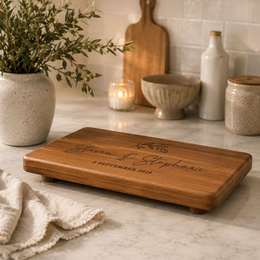 Personalised serving board with raised feet engraved with custom names displayed on a modern kitchen benchtop.