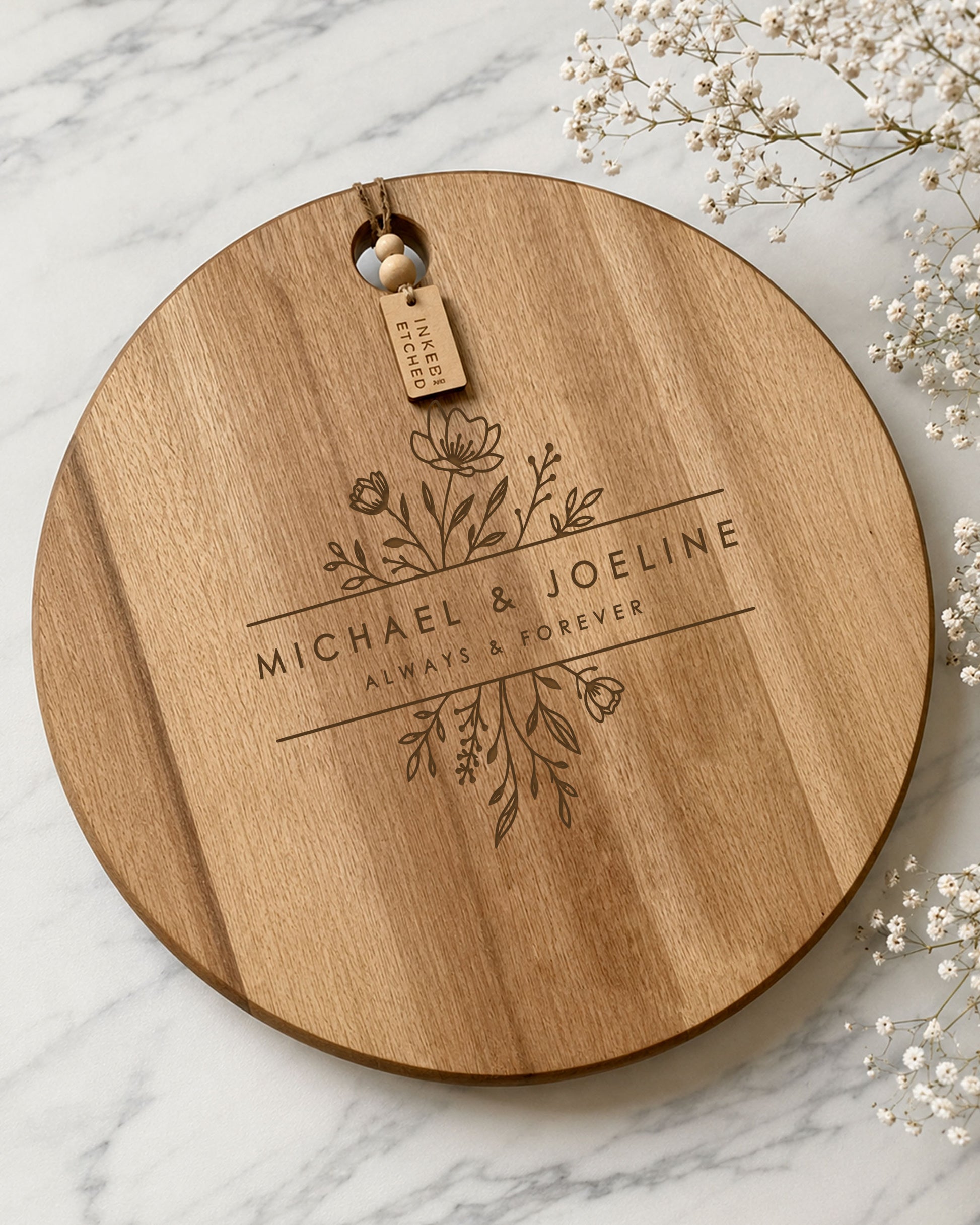 Personalised wedding cheeseboard engraved with floral design and custom names on a round acacia serving board.