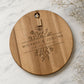 Personalised wedding cheeseboard engraved with floral design and custom names on a round acacia serving board.