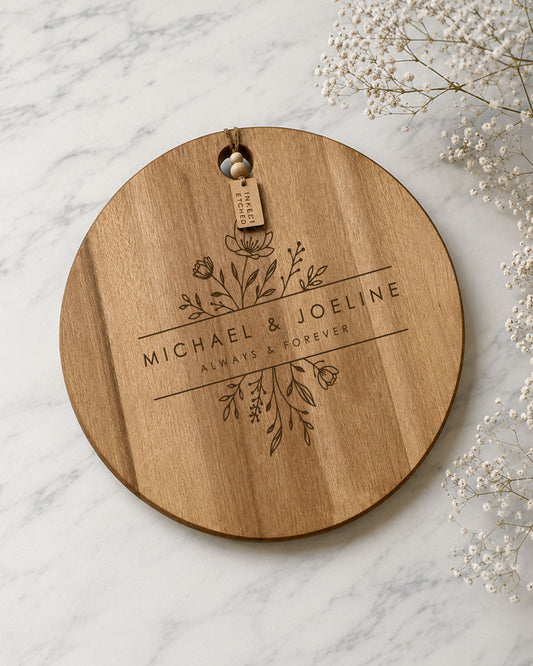 Personalised wedding cheeseboard engraved with floral design and custom names on a round acacia serving board.