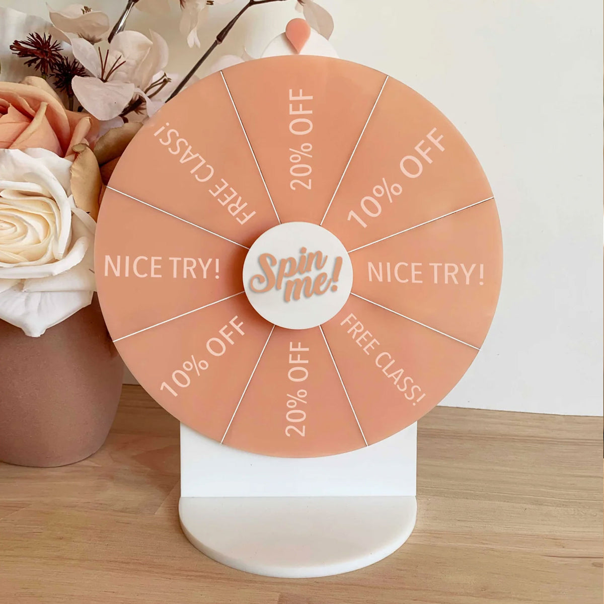 Peach printed Spin The Wheel with Spin Me centre and Pilates prizes, displayed beside flowers.