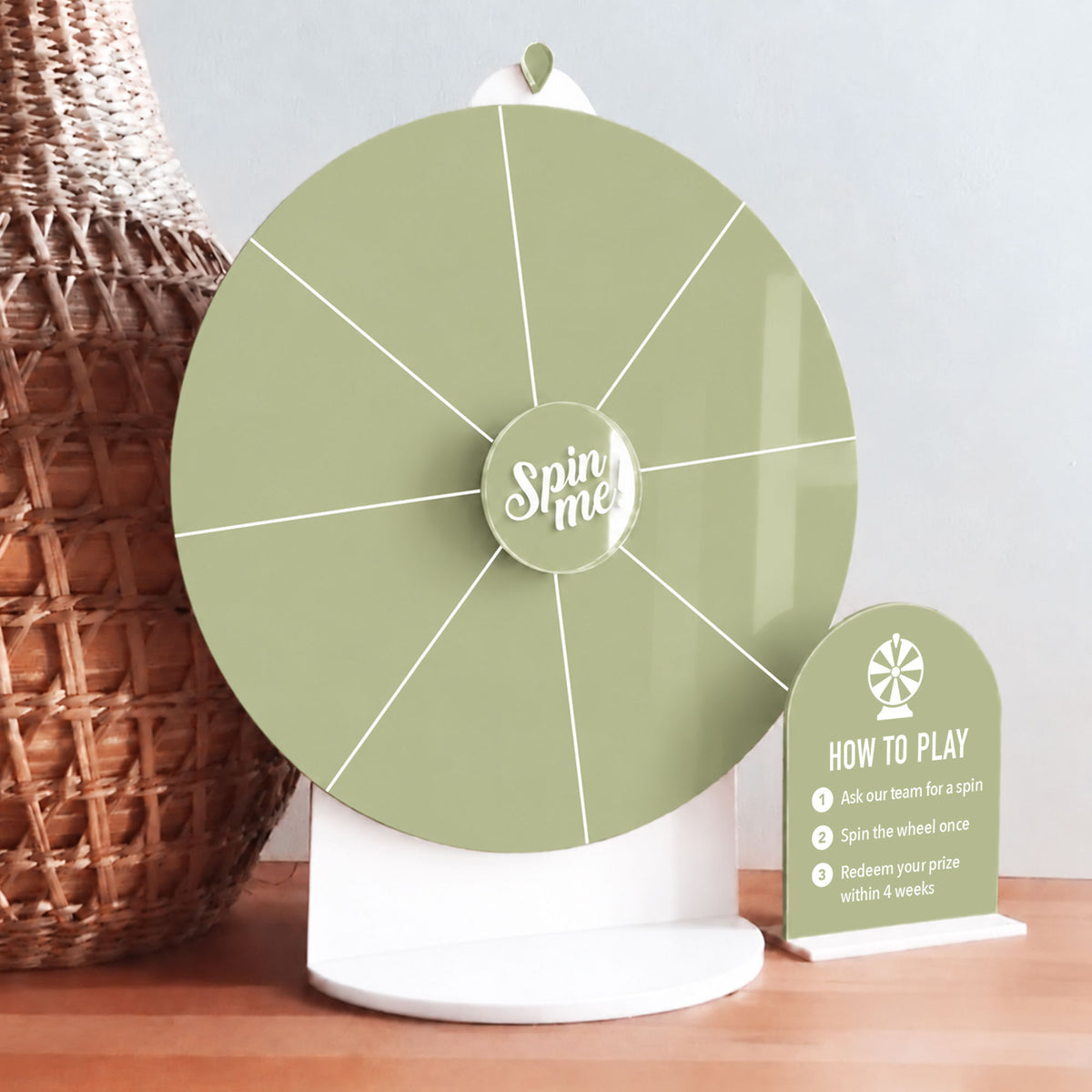 Green acrylic Spin The Wheel prize wheel with white section lines and a matching mini sign on a white stand.