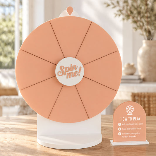 Front view of a peach acrylic Spin The Wheel with a white stand, “Spin Me” centre and matching instructions sign.