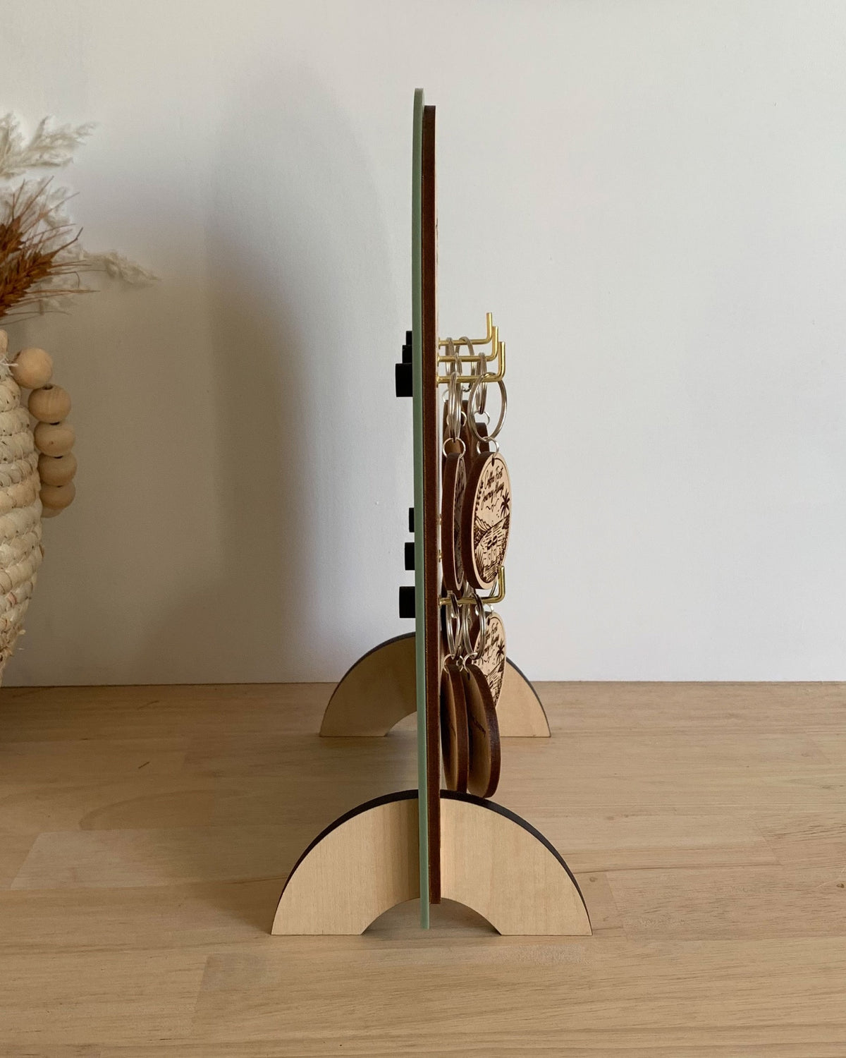 Side view showing the slim profile, hooks and timber feet of a wooden keyring display stand.